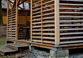 the pavilion in the park has sides made of planks shaped like slats or louvres. the pergola is airy...