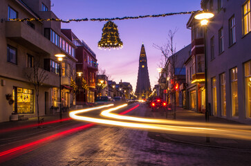 Twilight scene of a street in Iceland adorned with Christmas lights with the Hallgrímskirkja church in the background and light trails from moving cars
