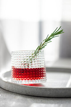 Elegant cocktail with cherry and apple juice mixed with vodka garnished with a fresh rosemary sprig presented on a circular tray