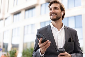 Confident young businessman using cell phone and drinking coffee in the city.