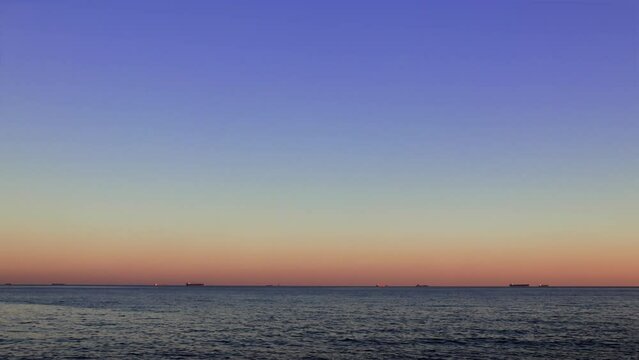 Ships anchored in roadstead against calm sea waves at sunset. Serene sunset, tranquil sea, ships on roadstead. Sunset view of ships on roadstead, calm sea waves