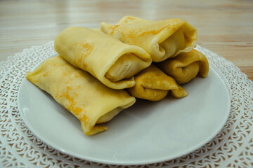 Five golden homemade pancakes with wrapped filling on a white plate