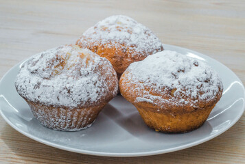 Three large shortbread cupcakes sprinkled with sweet powdered sugar on a white plate.