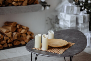 Cozy indoor setting with candles on a table, surrounded by wrapped gifts and firewood. The white tiled floor contrasts with the dark table.