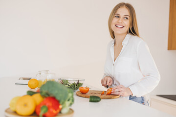 A happy cute blonde woman is preparing a salad in the kitchen