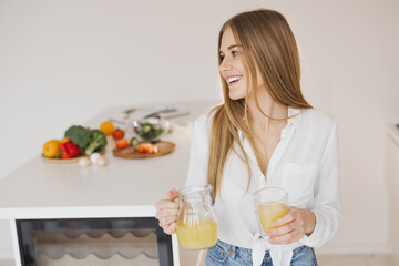 Obraz na płótnie Canvas A happy cute blonde woman drinks orange juice in the kitchen