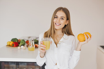 A happy cute blonde woman drinks orange juice in the kitchen