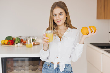 A happy cute blonde woman drinks orange juice in the kitchen