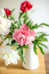 A bright room adorned with a vase of white and red flowers, including peonies on the table. The minimalistic and cozy interior highlights the flowers, making them a perfect gift