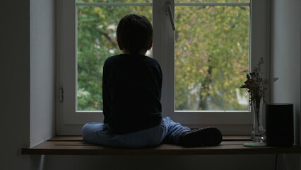 Back of Child sitting by window during winter season looking at snow fall. Melancholic concept young boy daydreaming staring at view from apartment window © Marco