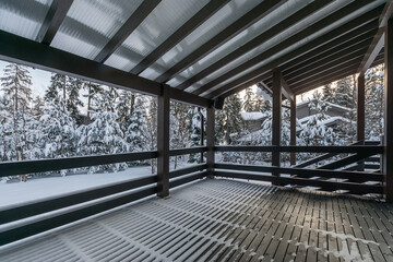 A spacious wooden terrace with a canopy surrounded by snow-covered fir trees on a clear winter day.