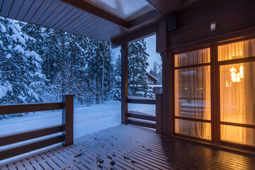 Beautiful view of the snow-covered forest from the terrace of a wooden house. It's twilight time....