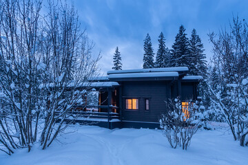 Winter evening. Light from the windows of a wooden house on the background of a snow-covered...