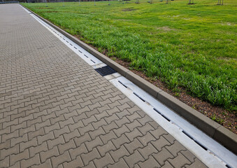 Slotted pipes drain rainwater and oil substances, drips from paved surfaces. concrete products at the curb interlocked paving tiles. sewage pipes hidden under the surface, hydroplaning - obrazy, fototapety, plakaty