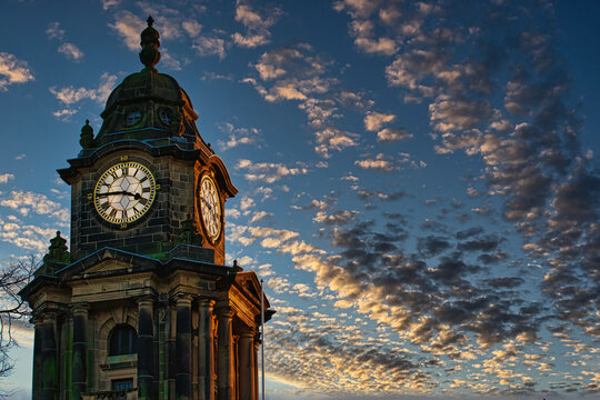 Historic clock tower silhouette against a dramatic sunset sky with scattered clouds in Lancaster.