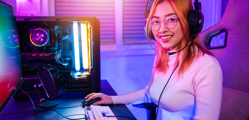 Smiling young woman wearing gaming headphones intend to do playing live stream games online at home looking to camera, Happy Gamer endeavor plays online video games tournament with computer neon light - obrazy, fototapety, plakaty