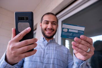 man using bank card with mobile phone to pay online for his order through mobile application