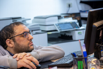 Book shop owner with printers in the background for printing services on his desk