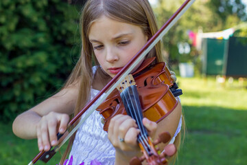 Cute little girl in white dress with flowers playing violin in the public park. Young artist © Jelena