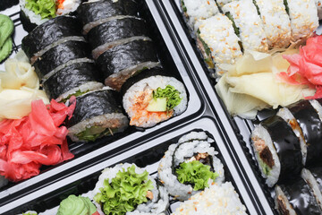 Takeaway sushi background. Uramaki California roll and futomaki. Japanese food isolated on black. Black sushi takeaway box closeup. Different various types of sushi. Lunch box texture. Sesame seeds.