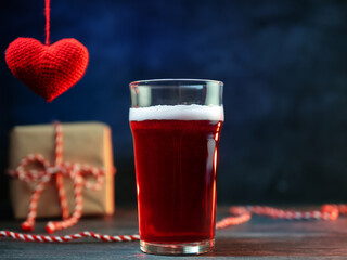 A glass of craft red sour ale, a surprise for Valentine's day. A gift box and a red heart. On a blue background with copy space