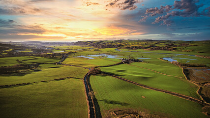 Breathtaking aerial view of a vibrant sunset over rolling green hills with a winding road and...