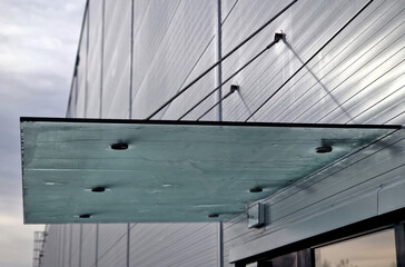 Fototapeta premium Glass roof above entrance industrial building with metal cladding of facade. thick-walled glass panel hangs above the door on metal rods with round targets holders, frosted, stainless steel, blue