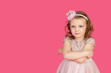 Obraz na płótnie Canvas Serious funny little girl in pink dress arms crossed at pink backdrop, posing serious looking. Lovely kid lady coquette expressing emotion, studio shot. Child image emotion concept. Copy ad text space
