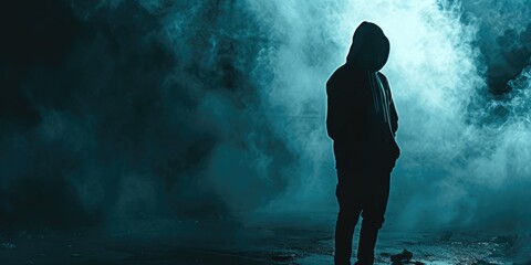 Silhouette of a man wearing a hoodie standing in a dark background - obrazy, fototapety, plakaty