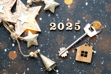 House key with keychain cottage on festive black background with stars, lights of garlands. New Year 2025 wooden letters, greeting card. Purchase, construction, relocation, mortgage, insurance