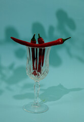Hot red chili peppers on the glass, on blue background with shadows.