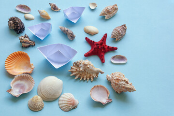 Different sea shells, starfish and white paper boats on blue. Copy space. Summer holidays and travel background