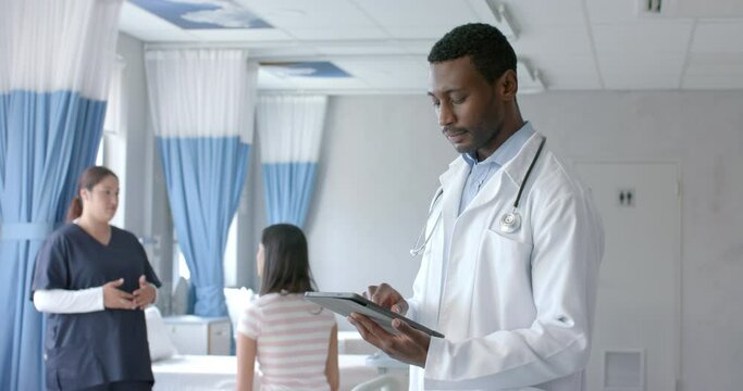 Portrait of african american male doctor using tablet and smiling in ward, copy space, slow motion