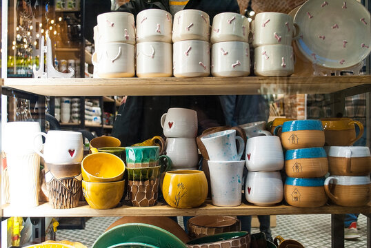 Bright multi-colored ceramic dishes in a store window. Cups of various shapes are neatly arranged on the shelf