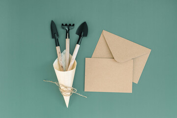 Three gardening tools in a wooden cone and an empty envelope on green.