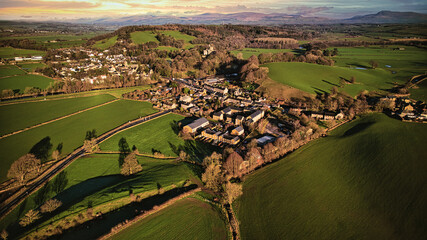 Aerial view of a quaint village surrounded by green fields and trees with a scenic landscape in the...