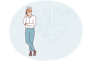 Young creative man project manager stands cross-legged and touches head thinking about future development of company. Startup employee guy posing near wall with stickers. Flat vector illustration