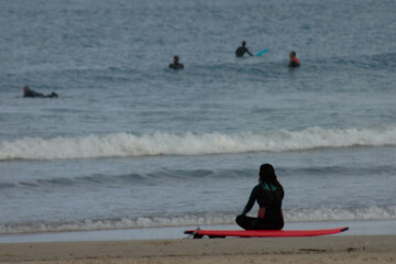 A young woman rests on the sand watching her windsurfing partners