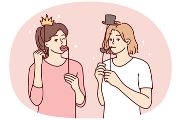 Girl friends with funny masks for photo shoot during house party or holiday carnival. Young casual women put cardboard lips and smoking pipe or crown with hat on their face. Flat vector illustration