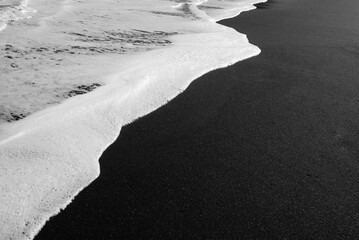 Mostly blurred black sand beach with white foam of sea waves background