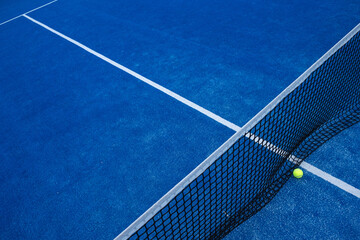 elevated view of the net of a blue paddle tennis court and a ball.