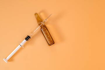 Small full syringe with needle on peach background. Next to it is the vial of medicinal liquid....