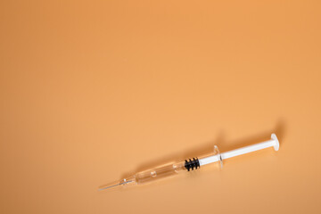 Small full syringe with needle on peach background. Copy Space.