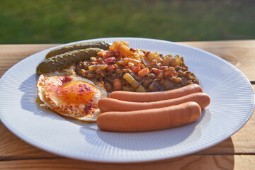 Delicious pork sausages with sunny side up egg, pickled sweet and sour cucumber and lentil mash served on white plate in the garden restaurant. Simple but tasty dish from cuisine of Czech Republic.
