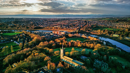 Aerial view of a cityscape at sunset with a prominent cathedral, lush green parks, and a river...