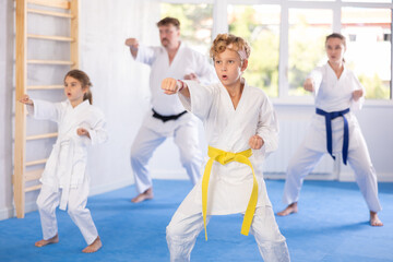 Concentrated tween boy in white kimono practicing punches in gym during family martial arts workout...