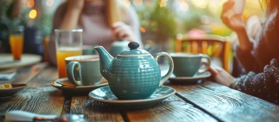  Unseen people enjoy hot drinks from stylish teapot and cups on a beautiful table. © Emin