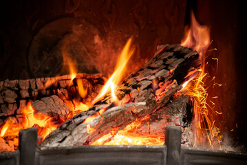 Burning ash tree logs in a home fireplace. Red flame tails, white ash, picturesque sparkles in...