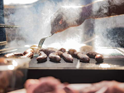 Unrecognizable man grilling sausages on grill rack covered by smoke