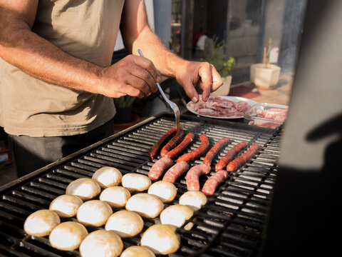 Unrecognizable man grilling sausages on grill rack